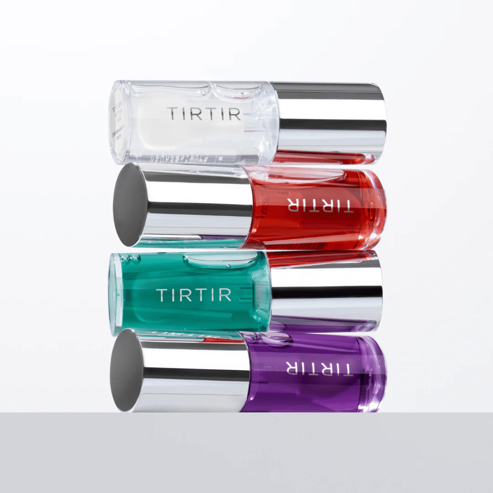 Fire TIRTIR My Glow Lip Oil i forskellige farver – gennemsigtig, rød, grøn og lilla – stablet på hinanden med sølvfarvede låg mod hvid baggrund.