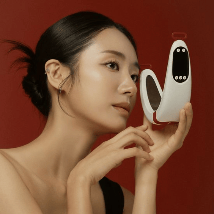 Model holder Beaund Nmode Pro foran ansigtet mod en rød baggrund. Billedet fremhæver enhedens elegante design, digitale display og kompakte format.