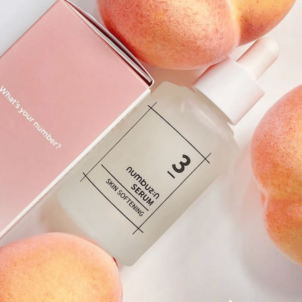Flaske med numbus:in No.3 Skin Softening Serum omgivet af ferskner og en lyserød æske med teksten "What's your number?".