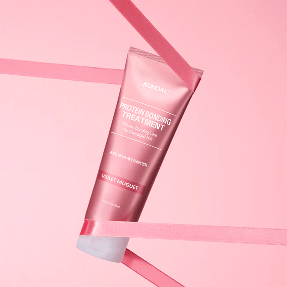 KUNDAL Protein Bonding Treatment Violet Muguet i lyserød tube 250 ml mod lyserød baggrund med dekorative bånd.