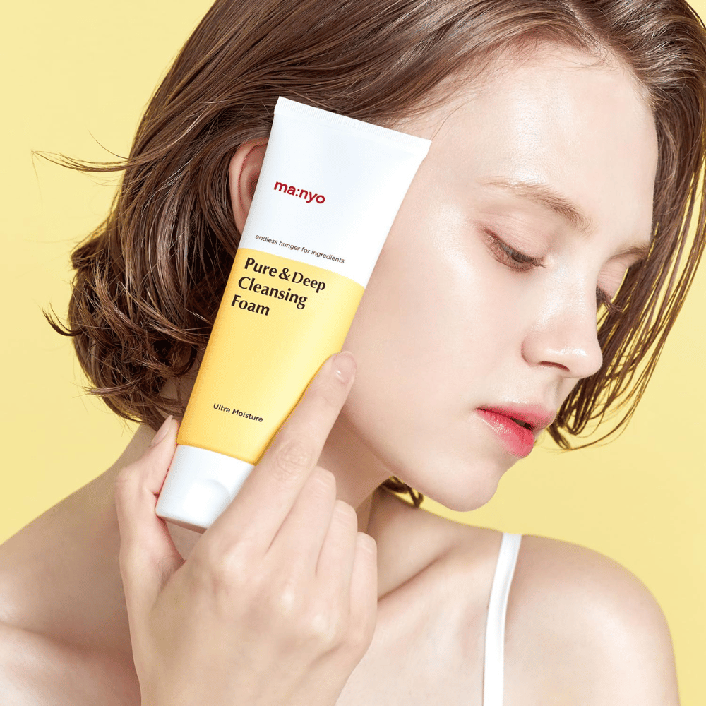 Kvinde med frisk, fugtet hud holder Ma:nyo Pure & Deep Cleansing Foam – mild ansigtsrens, der giver glød og balance med naturlige ingredienser.