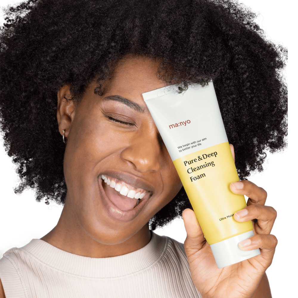 Kvinde med krøllet hår holder Ma:nyo Pure & Deep Cleansing Foam – en skånsom koreansk rens, der effektivt fjerner snavs og makeup uden at udtørre huden.