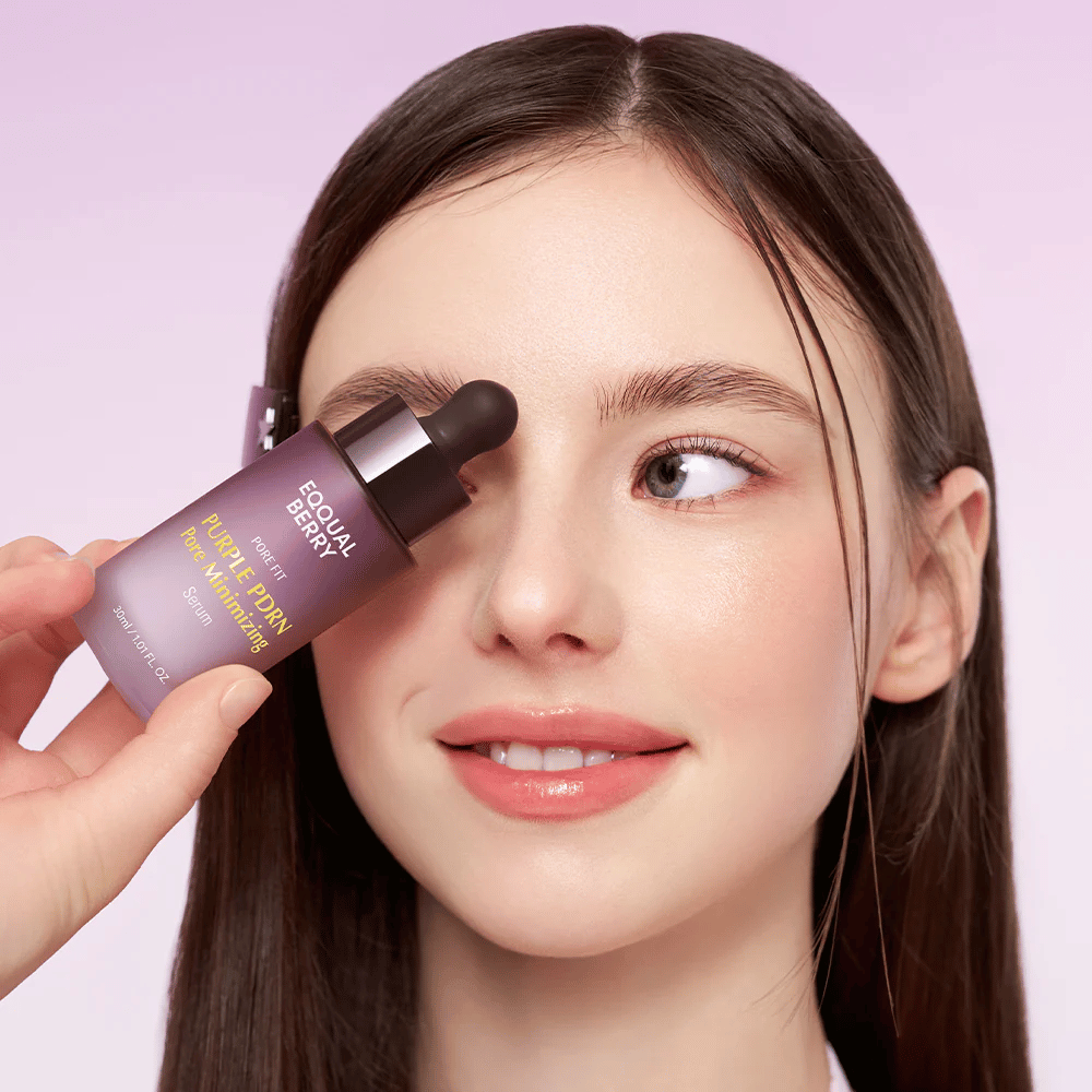 Ung kvinde med glat hud holder en flaske Equal Berry Purple PDRN Pore Minimizing Serum mod panden, mod en lys lilla baggrund.
