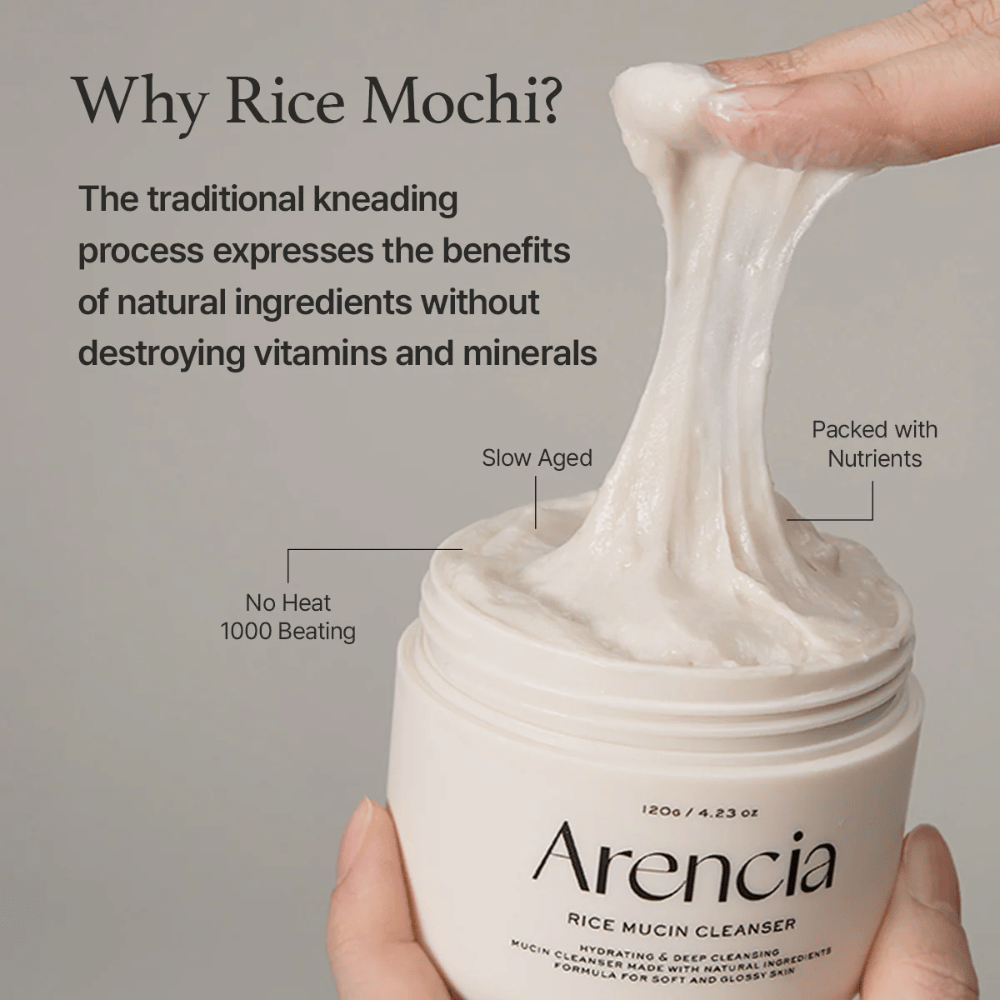 Hånd, der løfter en elastisk, hvid rengøringscreme op af en krukke mærket "Arencia Rice Mucin Cleanser". Teksten beskriver traditionel æltning, der bevarer næringsstoffer uden at ødelægge vitaminer og mineraler.