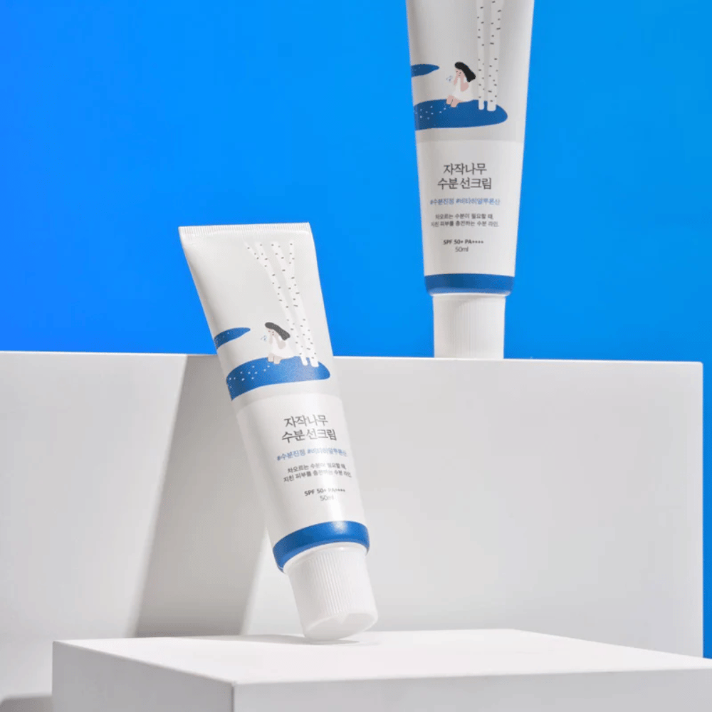 To tuber med Round Lab Birch Juice Moisturizing Sunscreen SPF50+ PA++++ 50ml som sidder ovenpå en blå baggrund.