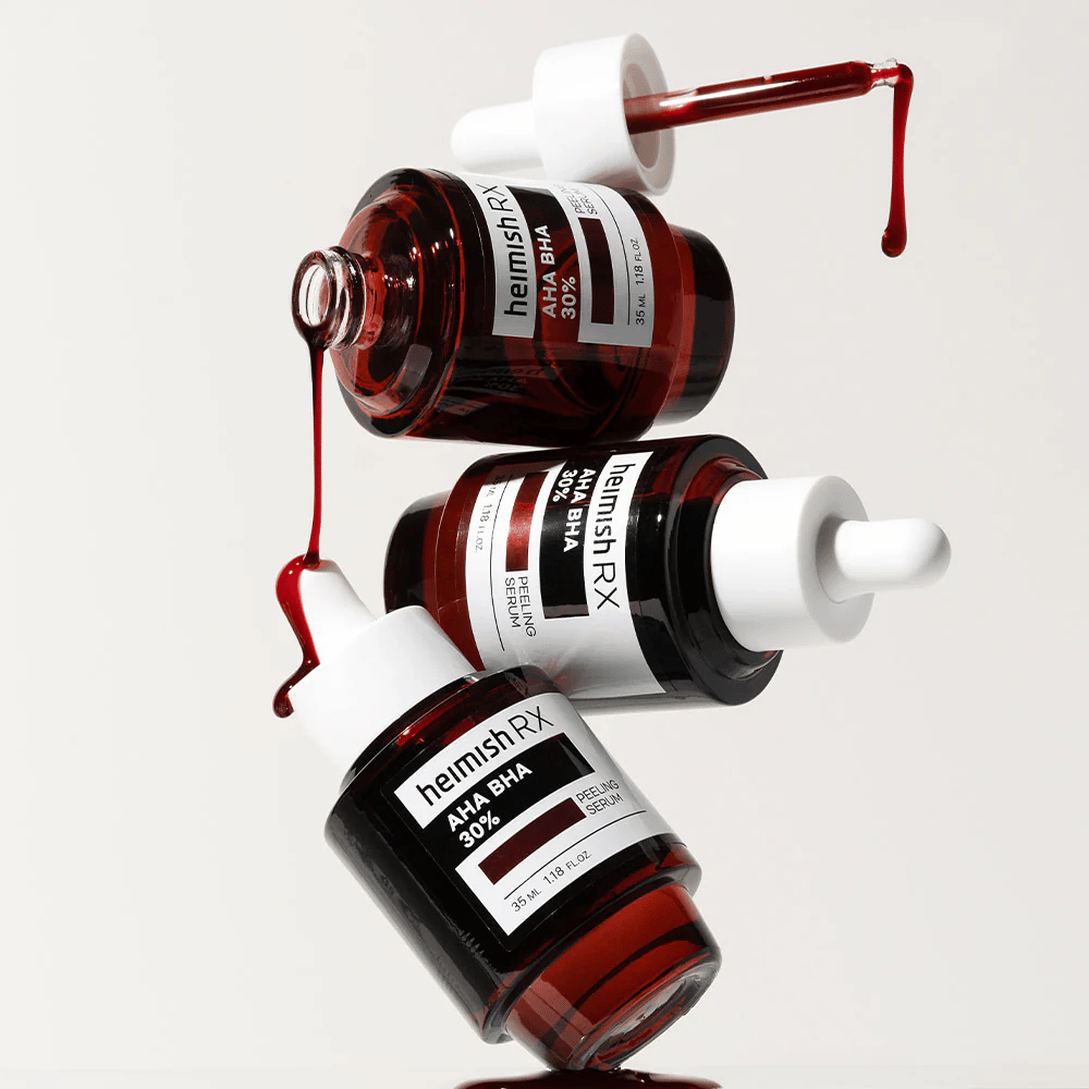 Tre flasker Heimish RX AHA BHA 30% Peeling Serum i en dynamisk komposition, med rødfarvet serum der drypper fra pipetterne.