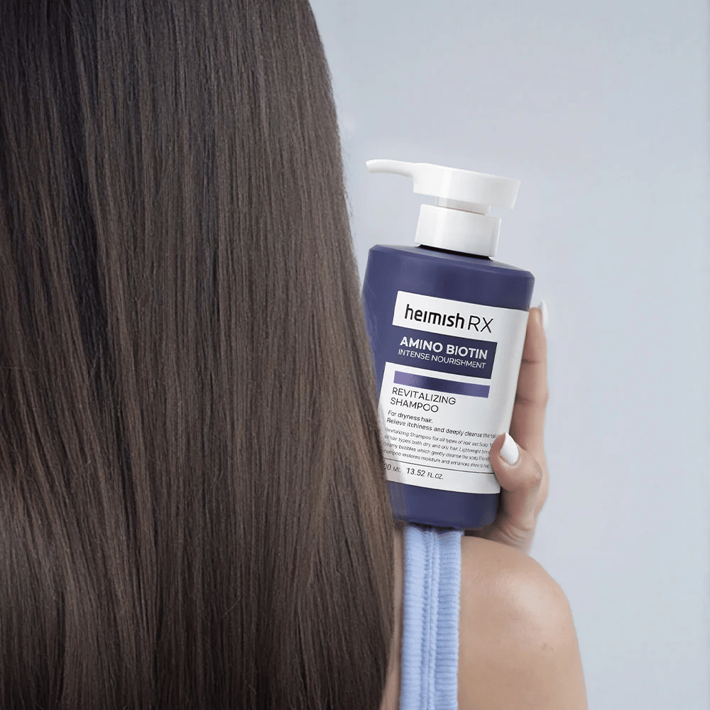 Heimish RX Amino Biotin Revitalizing Shampoo holdes i hånden mod langt, skinnende hår – viser resultatet af intensiv næring og fugt til tørt hår.