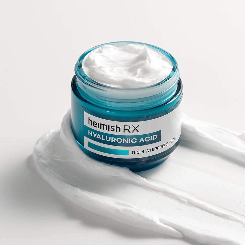 Heimish RX Hyaluronic Acid Rich Whipped Cream i en blå glasbeholder med rig og luftig konsistens, spredt på en hvid baggrund. Intensivt fugtgivende ansigtscreme med hyaluronsyre for dyb fugt og blød hud.