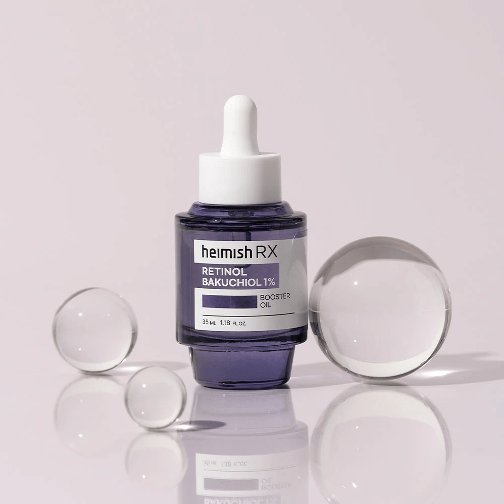 Heimish RX Retinol Bakuchiol Booster Oil 1% i en elegant lilla glasflaske med pipette. Olien er placeret på en reflekterende overflade med glaskugler rundt om, hvilket giver en luksuriøs og moderne følelse.