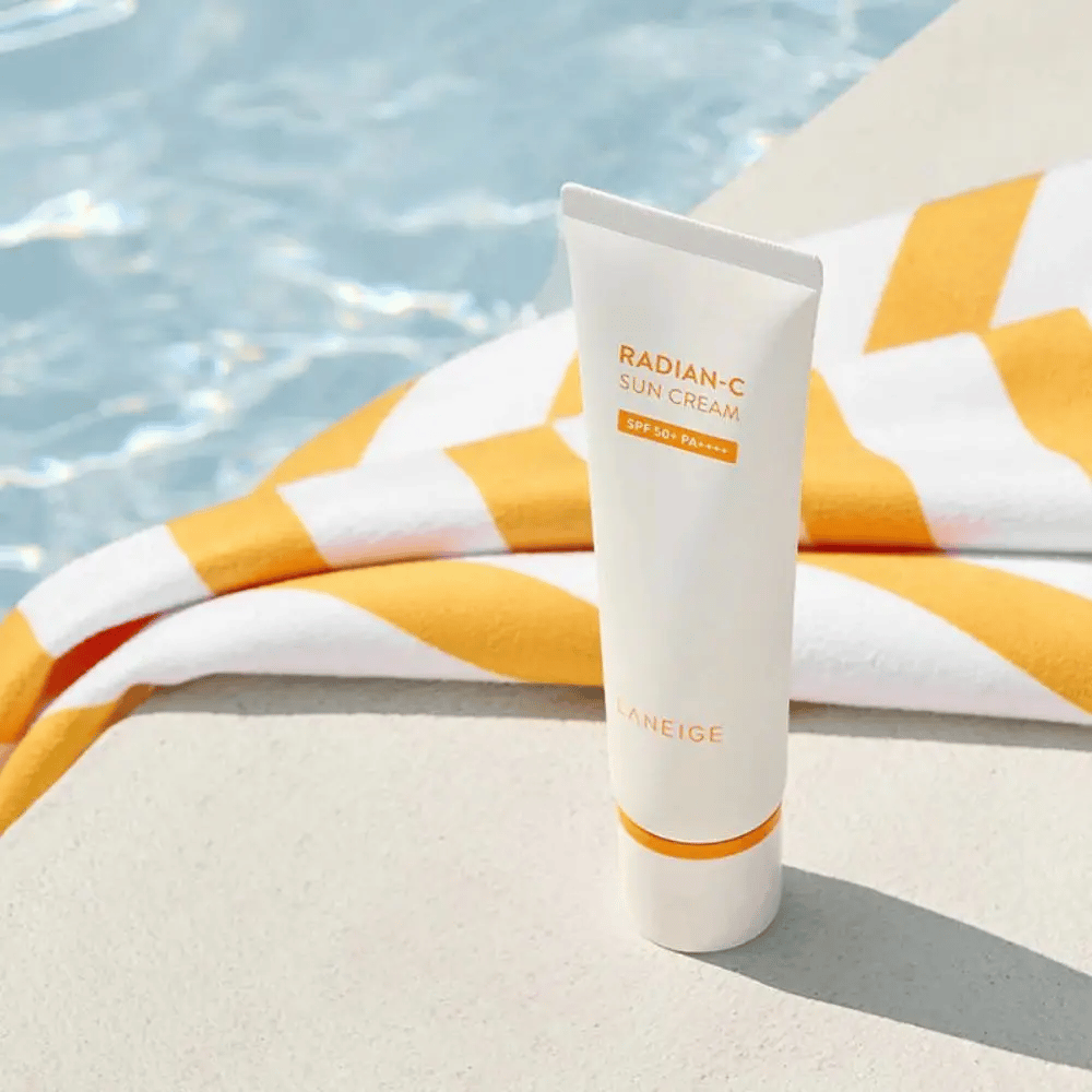 LANEIGE Radian-C Sun Cream står ved en poolkant med et gul- og hvidstribet håndklæde i baggrunden.