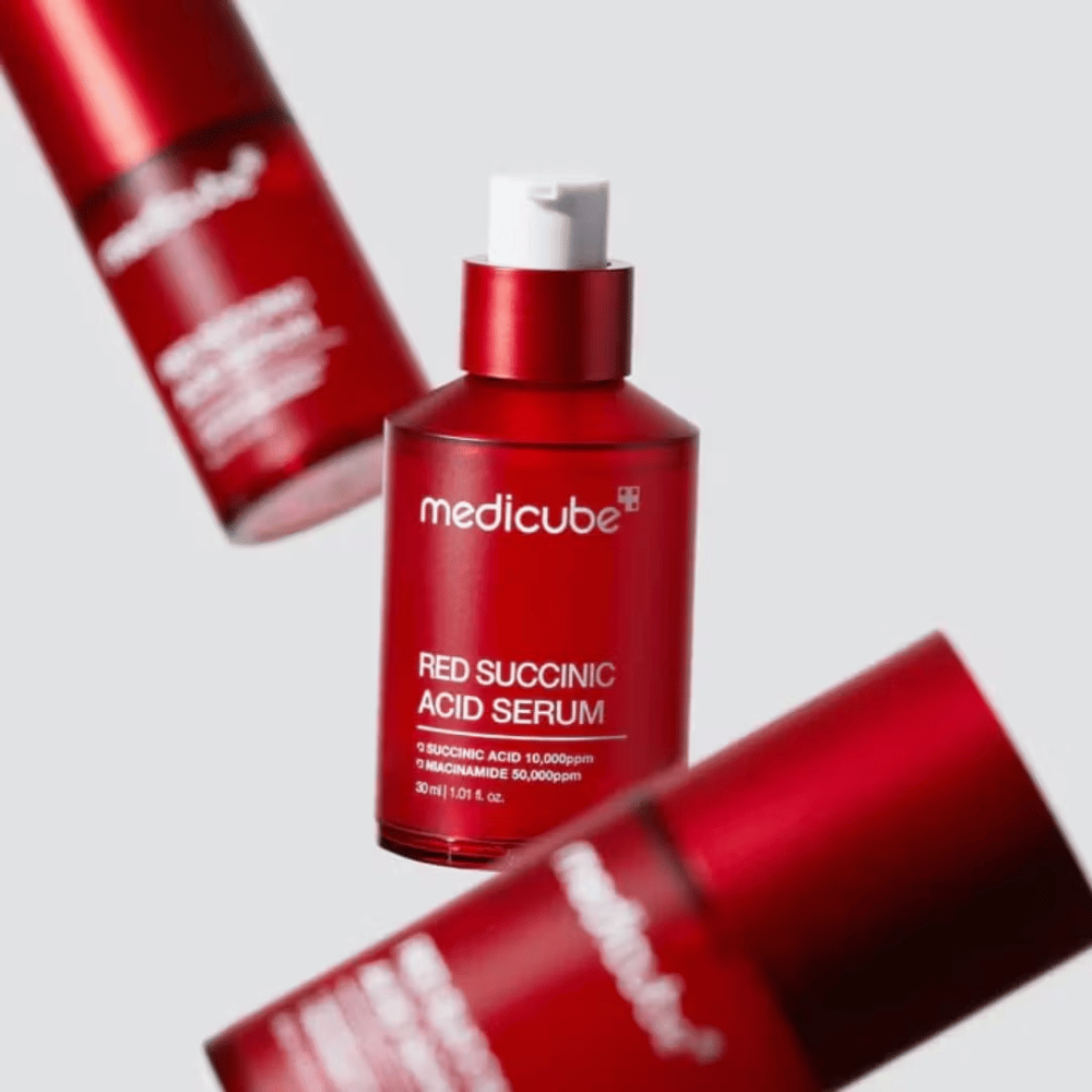 Medicube Red Succinic Acid Serum i rød pumpeflaske, omgivet af flere identiske flasker mod lys baggrund. Produktet indeholder succinic acid og niacinamide til behandling af akne og pigmentpletter.