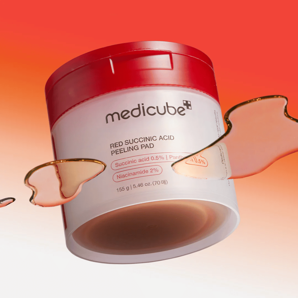 Medicube Red Succinic Acid Peeling Pad i en hvid og rød krukke, placeret mod en gradientbaggrund i rødt og orange. Produktet indeholder succinsyre og niacinamid til eksfoliering og hudforbedring. Flydende tekstur ses omkring krukken.