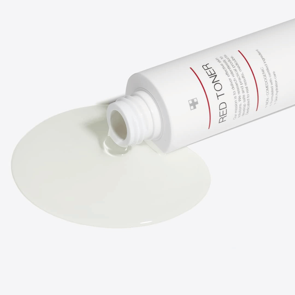 Åben flaske med medicube Red Toner der hældes ud på en hvid overflade – viser produktets lette og flydende konsistens.