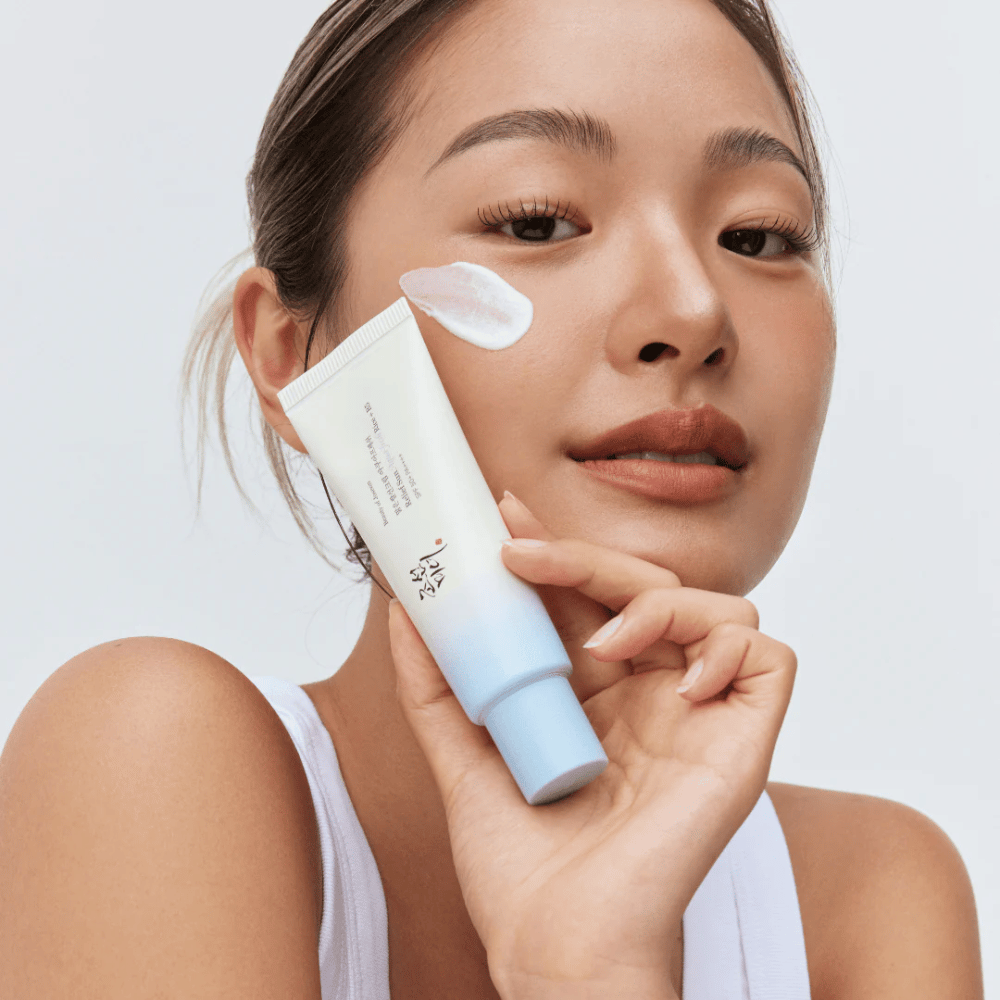 Kvinde holder Beauty of Joseon Relief Sun: Aqua-Fresh Rice + B5 solcreme og viser dens cremede konsistens på kinden. En let solbeskyttelsesprodukt, der fugter og beskytter huden med SPF 50+ PA++++.