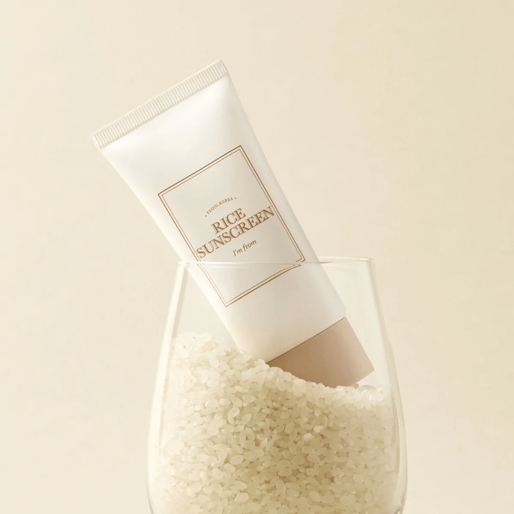 Tube med "I'm from" Rice Sunscreen, SPF50+ PA++++, placeret i et glas med riskorn.