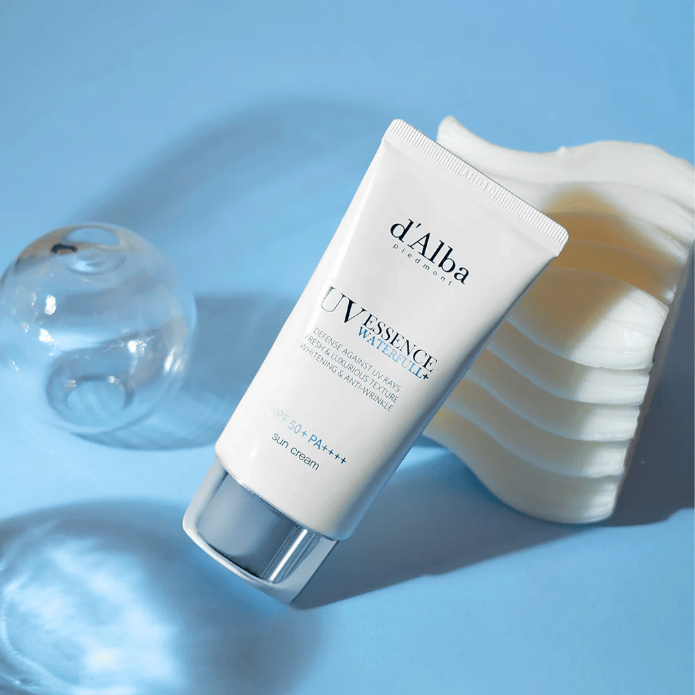 d'Alba UV Essence Waterfull+ Sun Cream med SPF 50+ PA++++ ligger mod en blå baggrund med lysreflektioner og dekorative elementer – fremhæver solcremens friske og fugtgivende egenskaber.