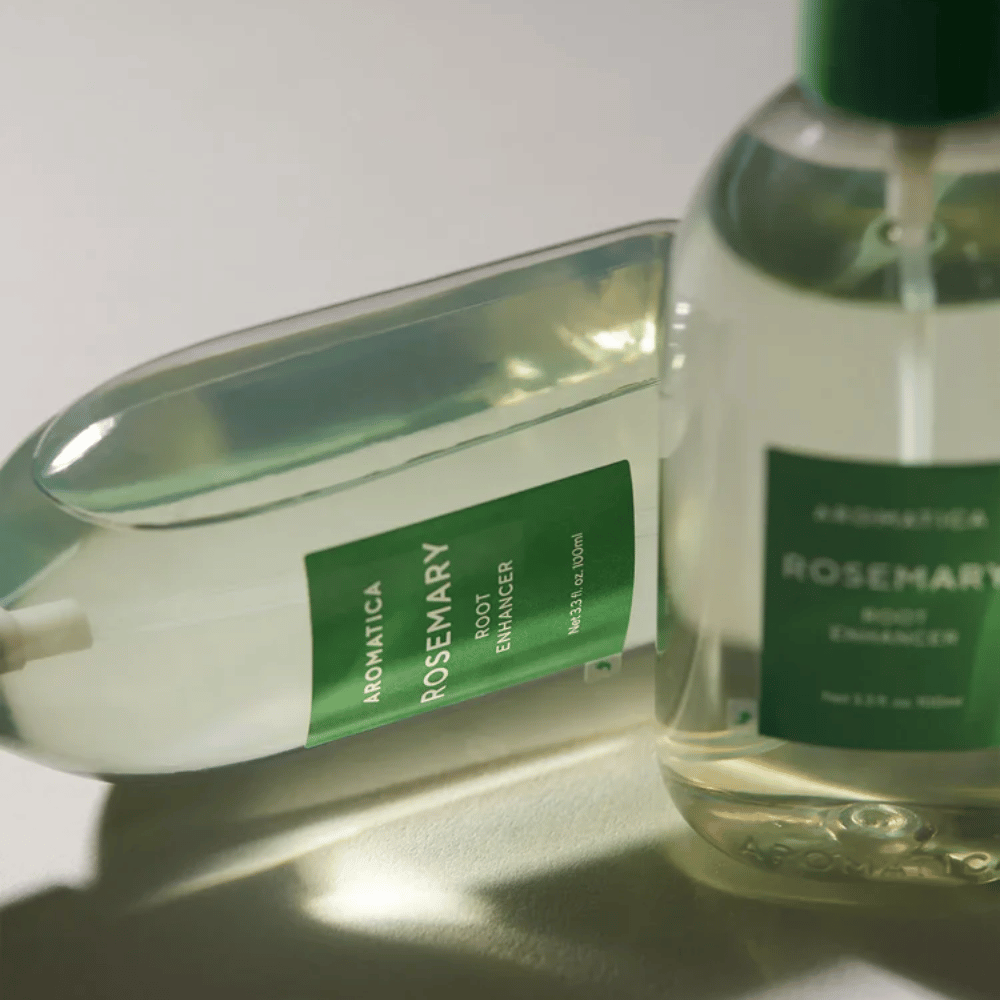 To AROMATICA Rosemary Root Enhancer-flasker med transparent beskyttelseshætte og grøn etiket. Nærbillede, som fremhæver produktets premiumdesign og naturlige hårplejekoncept.