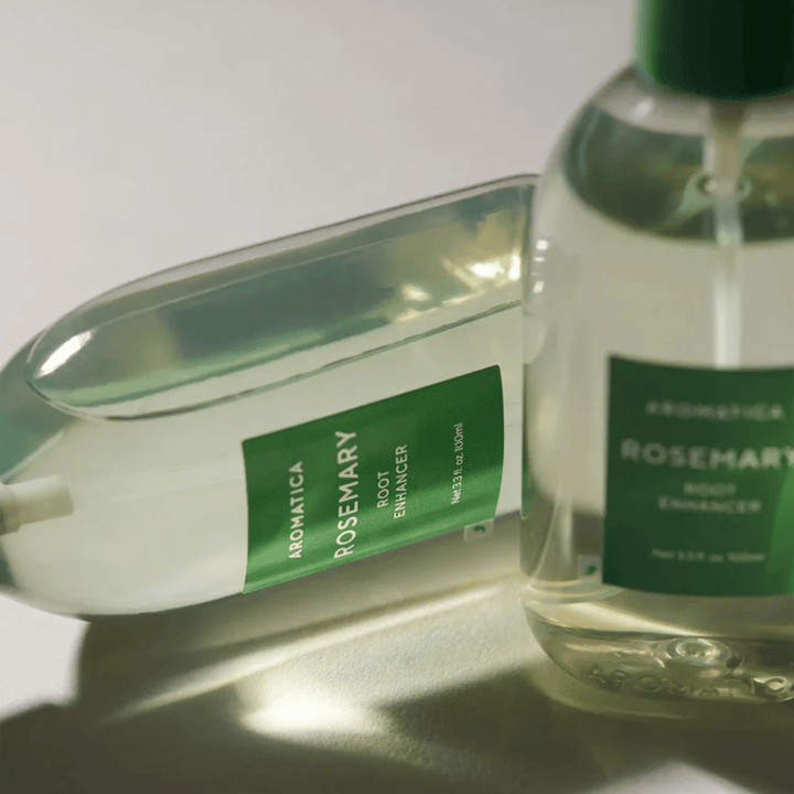 To AROMATICA Rosemary Root Enhancer-flasker med transparent beskyttelseshætte og grøn etiket. Nærbillede, som fremhæver produktets premiumdesign og naturlige hårplejekoncept.