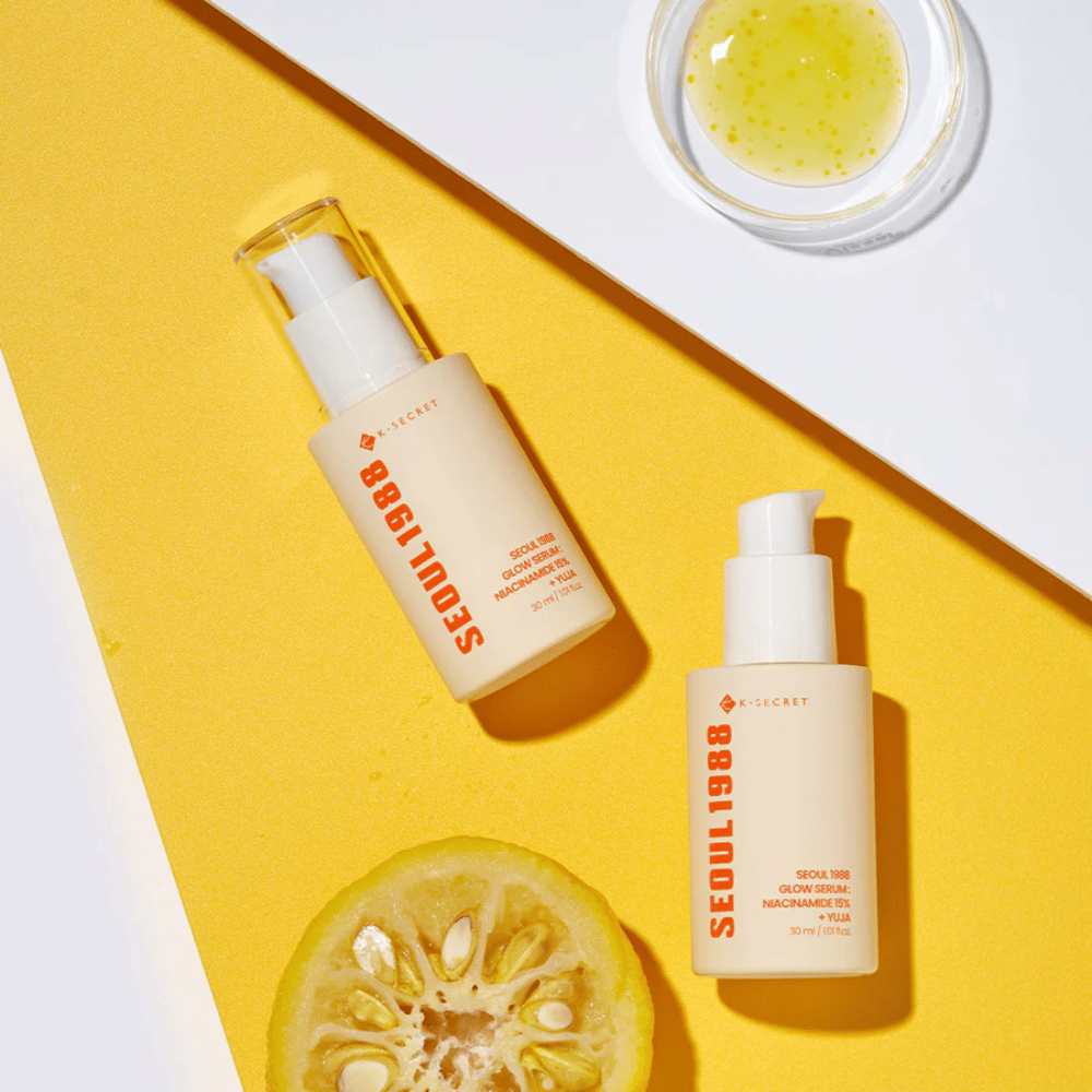 To flasker Seoul 1988 Glow Serum placeret på gul baggrund sammen med en skål med gul serum og en halveret citrusfrugt.