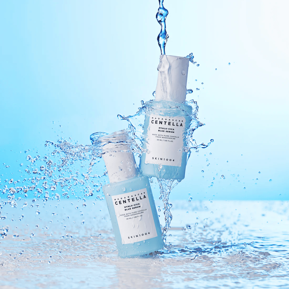 To flasker af SKIN1004 Madagascar Centella Hyalu-Cica Blue Serum rammes af en kaskade af vand mod en lyseblå baggrund.