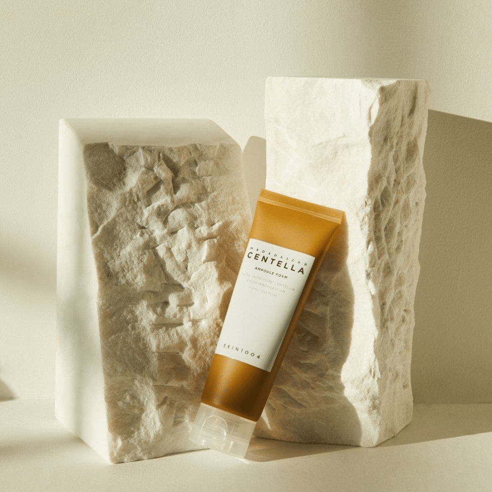 SKIN1004 Madagascar Centella Ampoule Foam stående mod lyse stenblokke i naturligt sollys, med sit brunhvide tubedesign og elegant minimalisme.