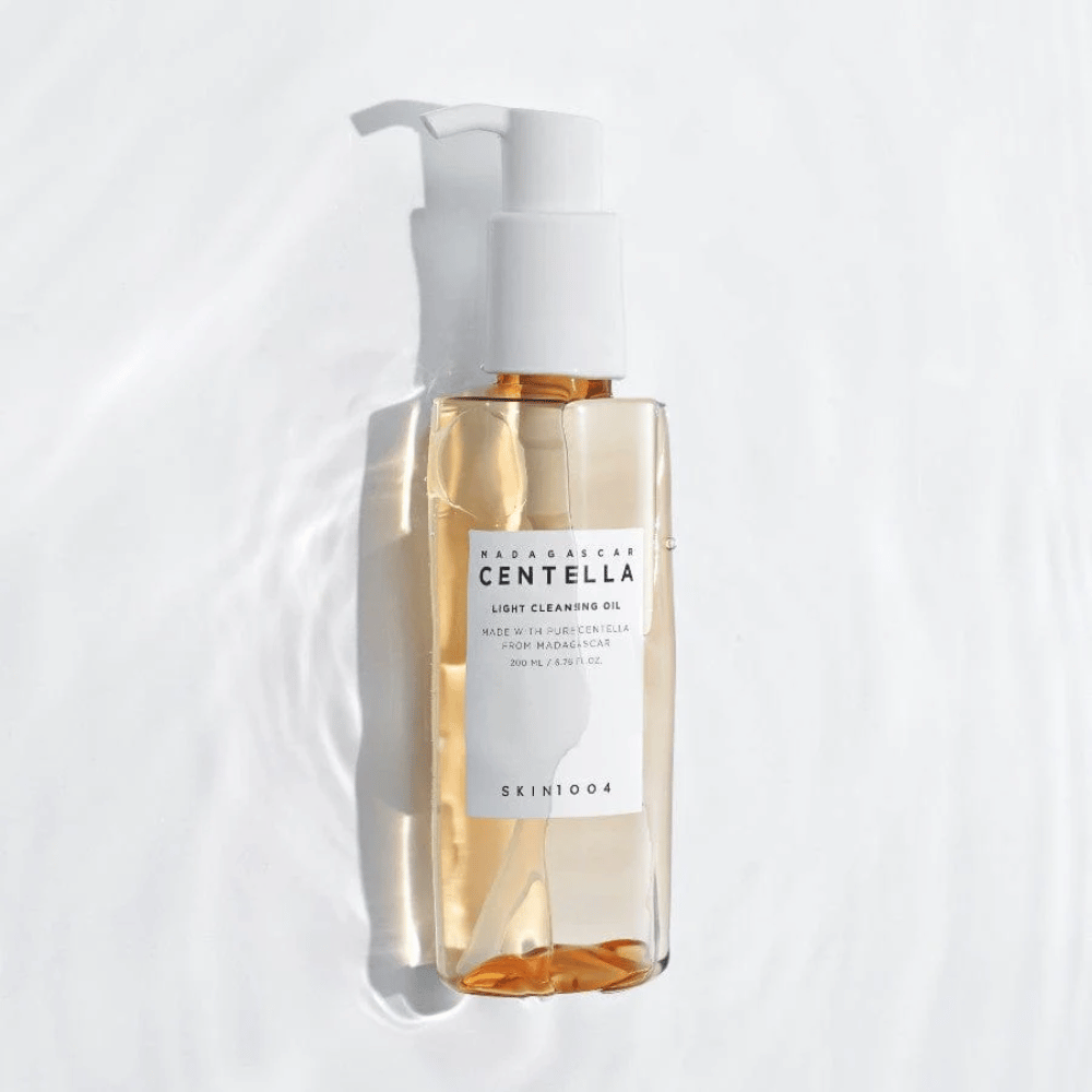 SKIN1004 Madagascar Centella Light Cleansing Oil på hvid baggrund med bløde vandreflekser, der fremhæver den transparente flaske og det gyldne indhold.