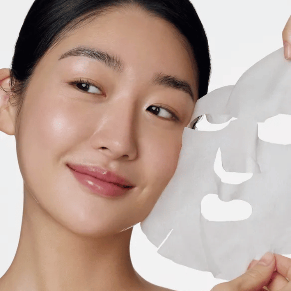 Billedet viser en person, der bruger en ansigtsmaske, specifikt en "Retinol Intense Daily Mask" fra Some By Mi. Masken er designet til daglig brug og indeholder retinol for at forbedre hudens tekstur, reducere fine linjer og give en mere jævn hudtone.