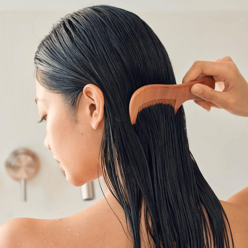 Person reder langt, vådt hår igennem med bred kam efter påføring af Heveblue Salmon Pullkeratin Centella Hair Treatment. Illustrerer udredende og blødgørende effekt for et glattere resultat.