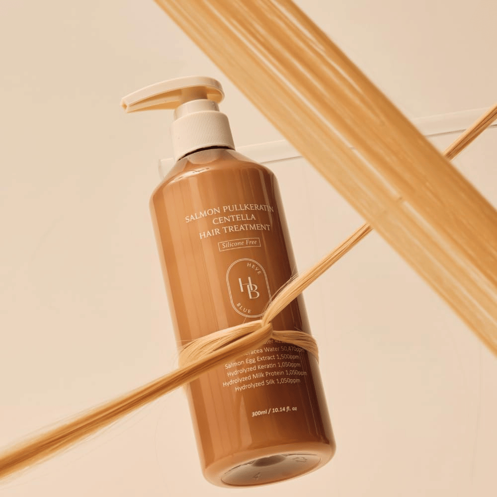 Heveblue Salmon Pullkeratin Centella Hair Treatment i brun flaske omgivet af hårtotter. Billedet fremhæver hårbehandlingens plejende egenskaber med fokus på glans, styrke og silkeblødt hår.