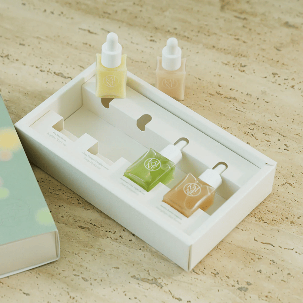 Fire farverige serumflasker fra KAINE Serum Discovery Kit med pipettekork, designet til at imødekomme forskellige hudbehov i en minimalistisk og stilren emballage.