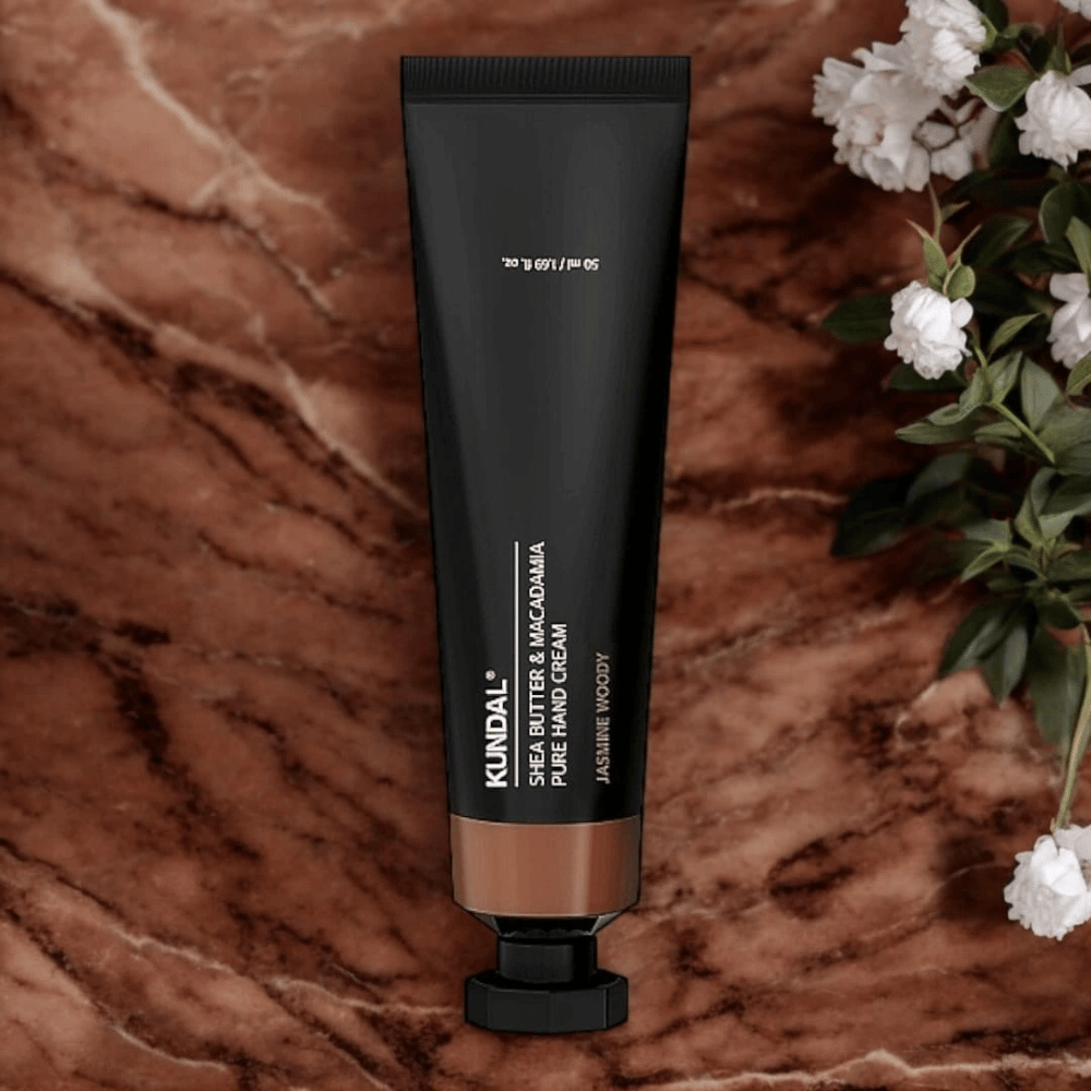 KUNDAL Shea Butter & Macadamia Pure Hand Cream Jasmine Woody placeret på marmor med blomster – nærende håndcreme, der plejer tørre hænder og giver en elegant jasmine woody-duft.