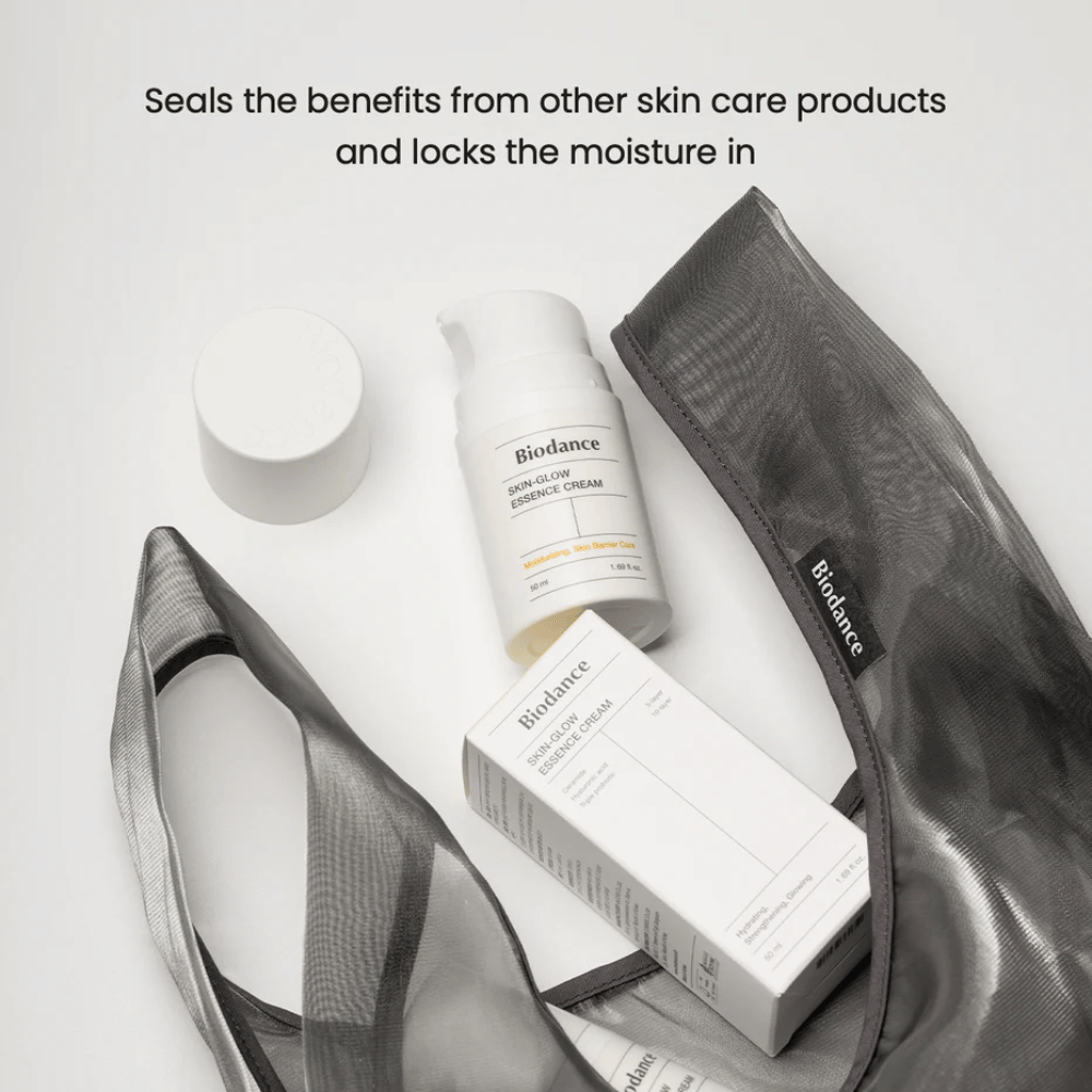 Biodance Skin-Glow Essence Cream stående i fokus sammen med produktemballage og en sort gennemsigtig toilettaske, med tekst ovenfor, der fremhæver cremens evne til at indkapsle fugt og forstærke effekten af andre hudplejeprodukter.
