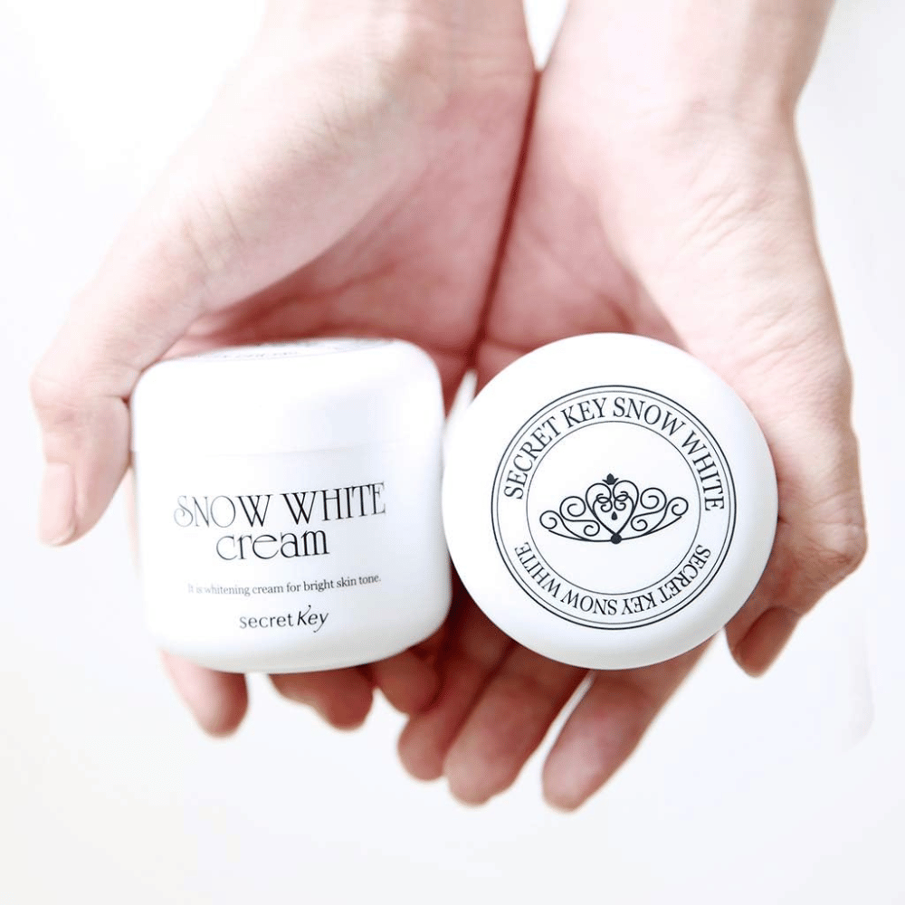 To krukker Secret Key Snow White Cream holdes i hænderne, en viser låget og en viser forsiden.