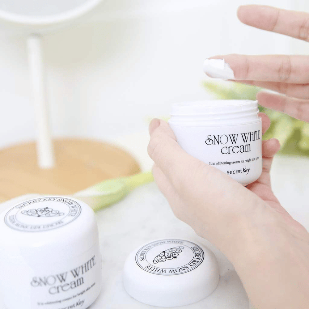 Hånd der tager hvid creme op fra en krukke Secret Key Snow White Cream på et sminkebord.