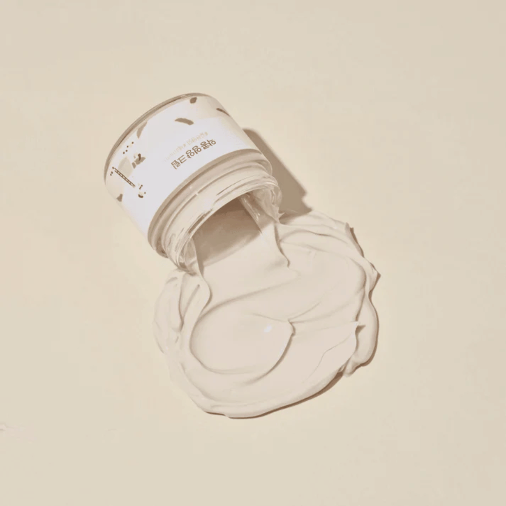 Mixsoon Soybean Nourishing Cream spildt ud af bøtten på en beige baggrund. Cremens fyldige konsistens viser dens intensive fugtgivende egenskaber.