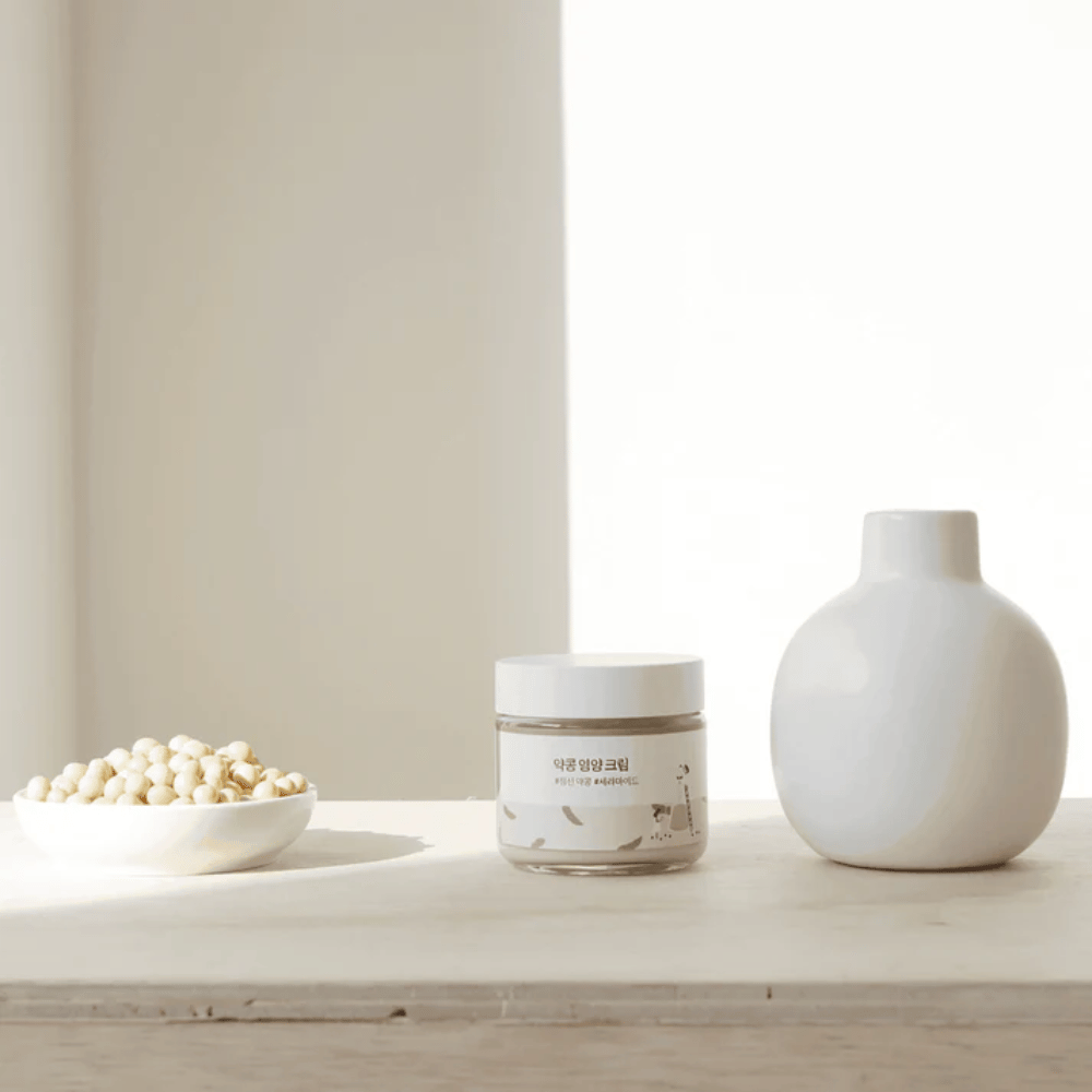 Mixsoon Soybean Nourishing Cream står på et træbord ved siden af en vase og sojabønner. En minimalistisk, fugtgivende creme med naturlige ingredienser.