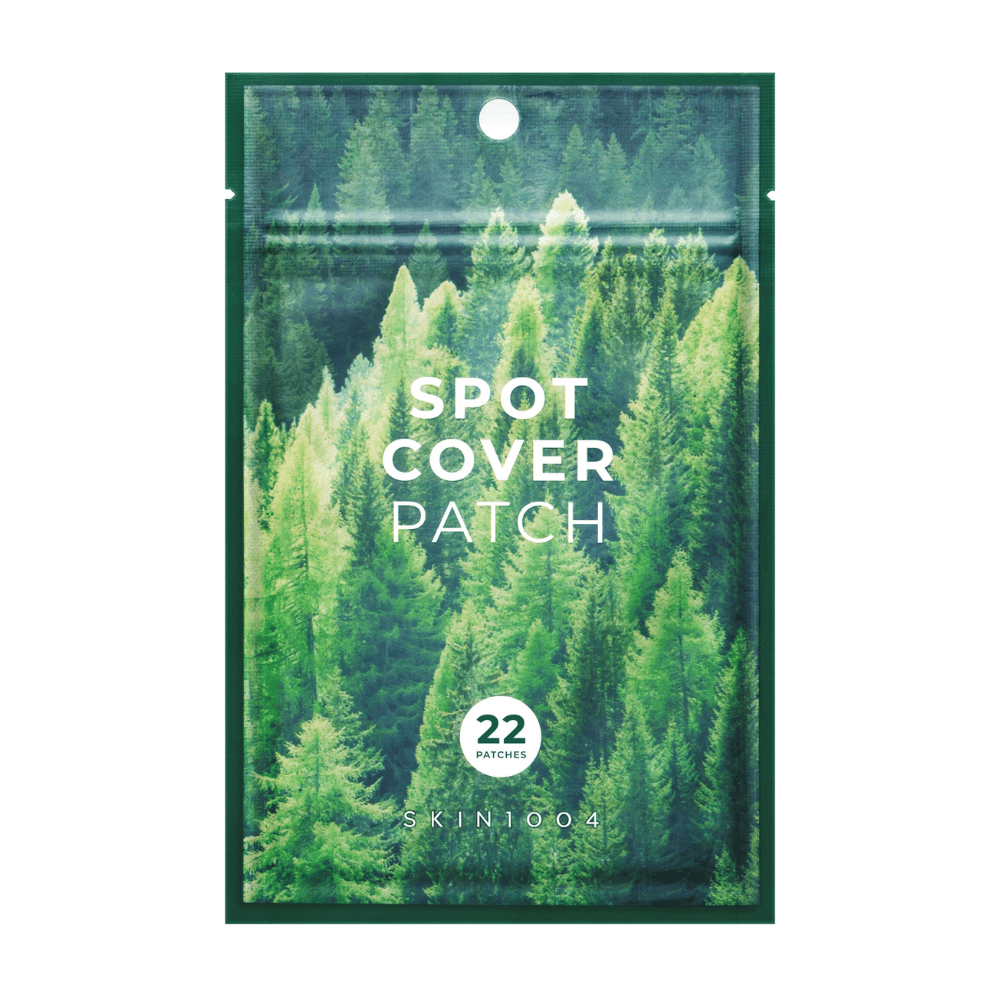 Emballage med "Spot Cover Patch" som indeholder 22 plastre, designet med et grønt skovmotiv. Teksten "SPOT COVER PATCH" er trykt i hvidt på forsiden, og en cirkel markerer antallet af plastre. Produktet er fra mærket SKIN1004.