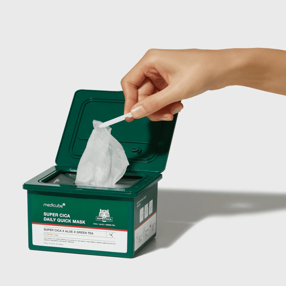 Grøn beholder med åbent låg viser medicube Super Cica Daily Quick Mask. En hånd trækker en arkmaske op med medfølgende pincet. Produktet indeholder Cica, aloe og grøn te, ideel til hurtig fugtighed og beroligende effekt.