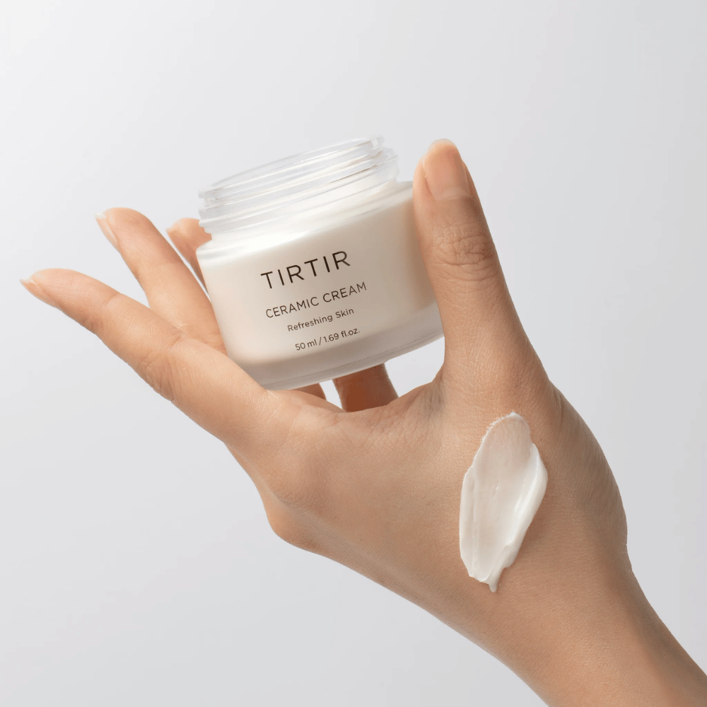 En hånd holder en krukke med TIRTIR Ceramic Cream. På håndryggen er en mængde af cremen blevet påført. Cremen ser ud til at være tyk og fugtgivende. Emballagen angiver, at indholdet er til "Refreshing Skin" og mængden er 50 ml / 1.69 fl oz.