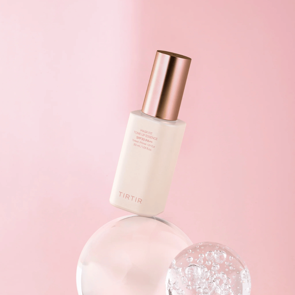 Billedet viser en flaske "TIRTIR MASK FIT TONE UP ESSENCE" med SPF30 PA++ mod en lyserød baggrund, hvilket giver en følelse af blødhed og femininitet.