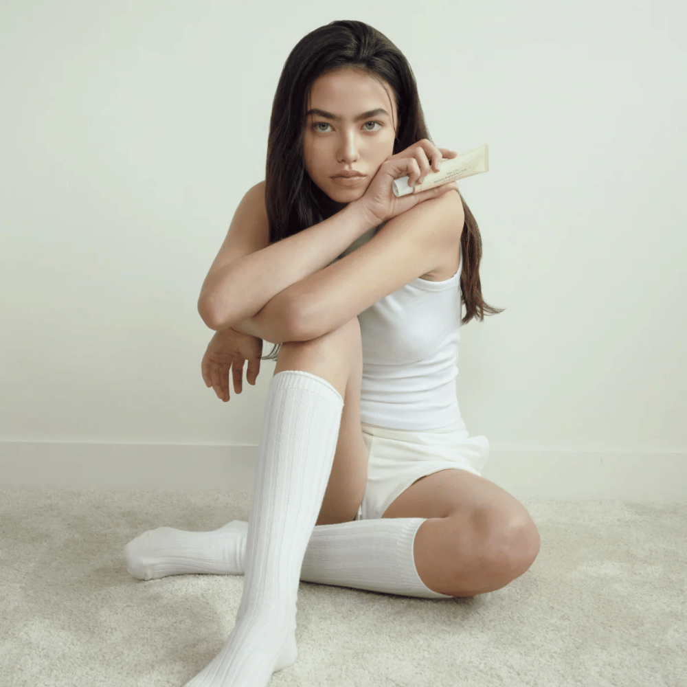 Lifestylebillede med model, der holder produktet i et lyst og minimalistisk miljø. Billedet formidler en ren, naturlig og rolig hudplejefølelse koblet til glow- og brightening-effekt.