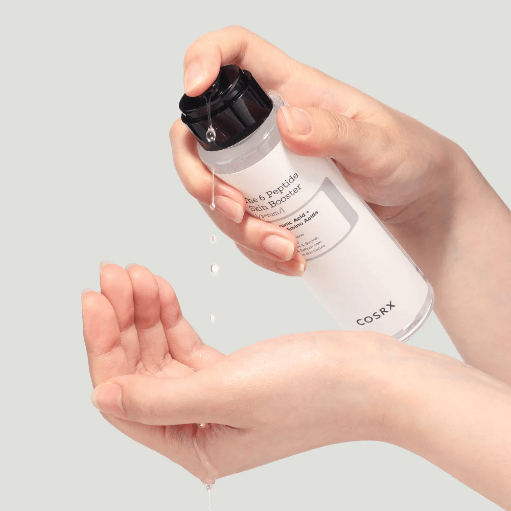 Hænder der hælder hudplejeprodukt ud fra en transparent flaske med teksten "The Peptide Skin Booster".