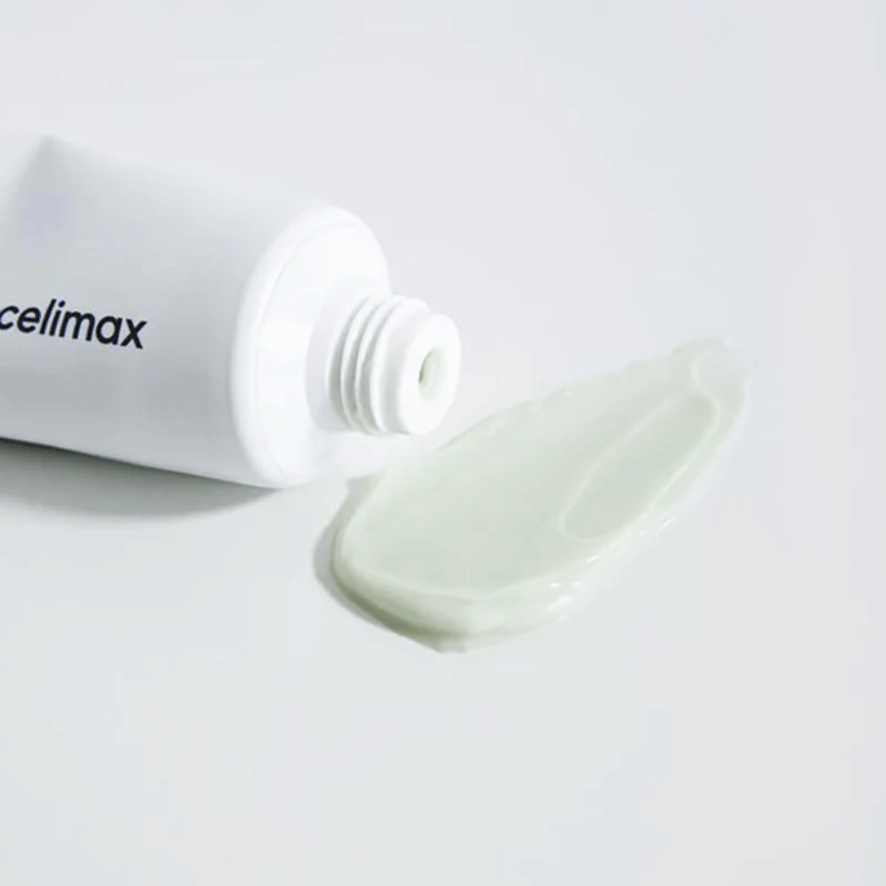 Celimax Noni Energy Repair Cream i en hvid tube med en lille mængde lysegrøn creme sprøjtet ud ved siden af tuben på en hvid overflade. Cremen er til at give næring og reparere huden.