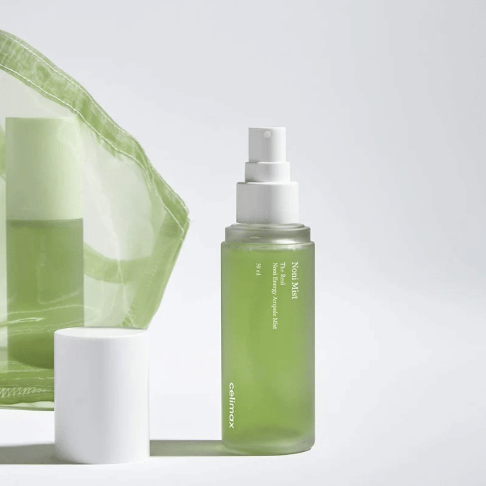En flaske med Celimax Noni Mist, en grøn sprayflaske med hvid pumpe, som står ved siden af et låg. Produktet er pakket i en gennemsigtig plastikpose og markedsføres som Noni Energy Ampule Mist.