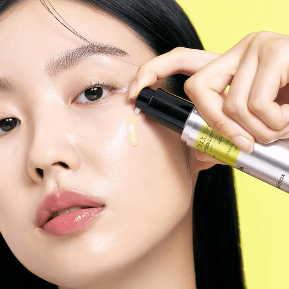 Model anvender The Vita-A Retinol Shot Tightening Serum fra Tiam nær øjenområdet, med fokus på hudens glød og serumets gule konsistens.