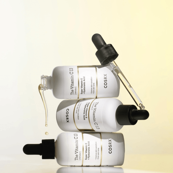 COSRX The Vitamin C 13 Serum med vitamin E og hyaluronsyre, tre flasker med pipette og dråber af C-vitaminserum mod ujævn hudtone og glød.