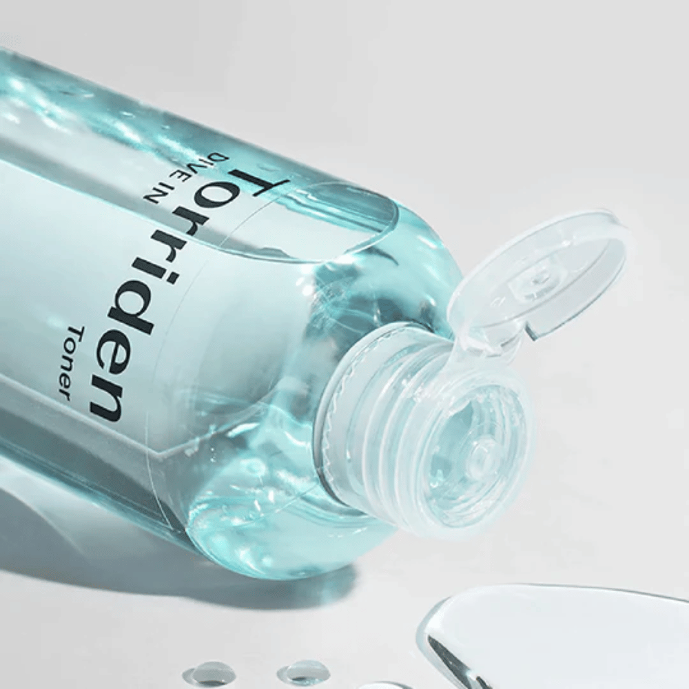En flaske DIVE-IN Low Molecule Hyaluronic Acid Toner 300ml ved siden af et glas vand, fremmer Torriden og fugtgivende.