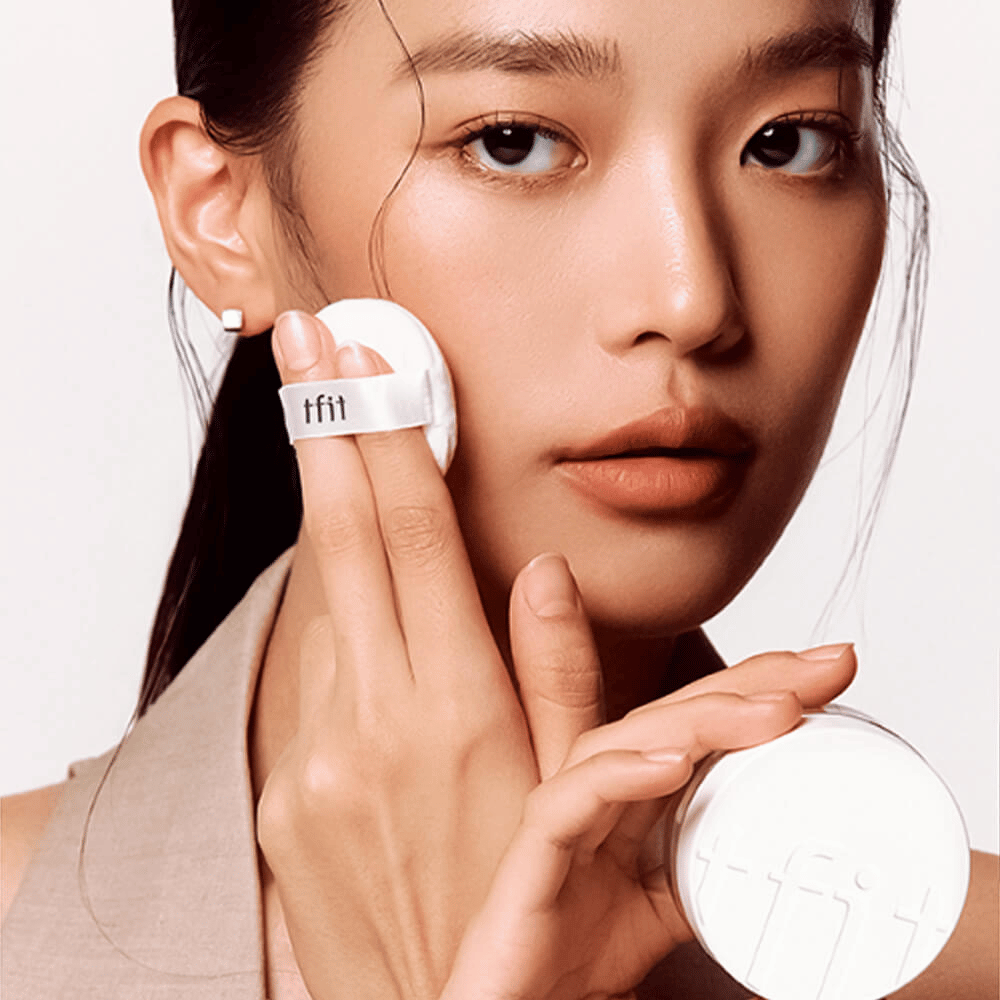 Kvinde anvender TFIT Translucent Set Finishing Powder #02 Skin Beige med en puff, holder i en hvid pudderdåse med TFIT-logo.