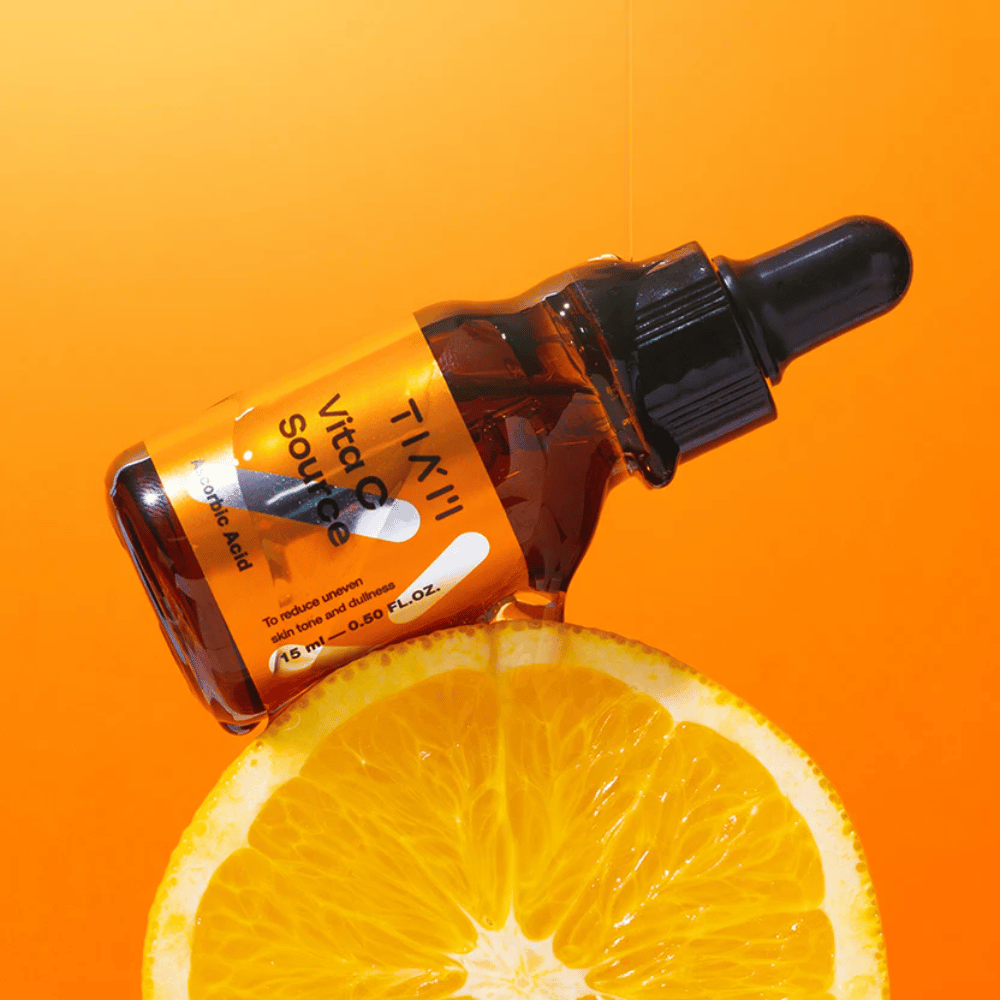 TIA'M Vita C Source-flaske placeret mod en appelsin og en orange baggrund, der symboliserer C-vitaminets friskhed og antioxidante effekt.