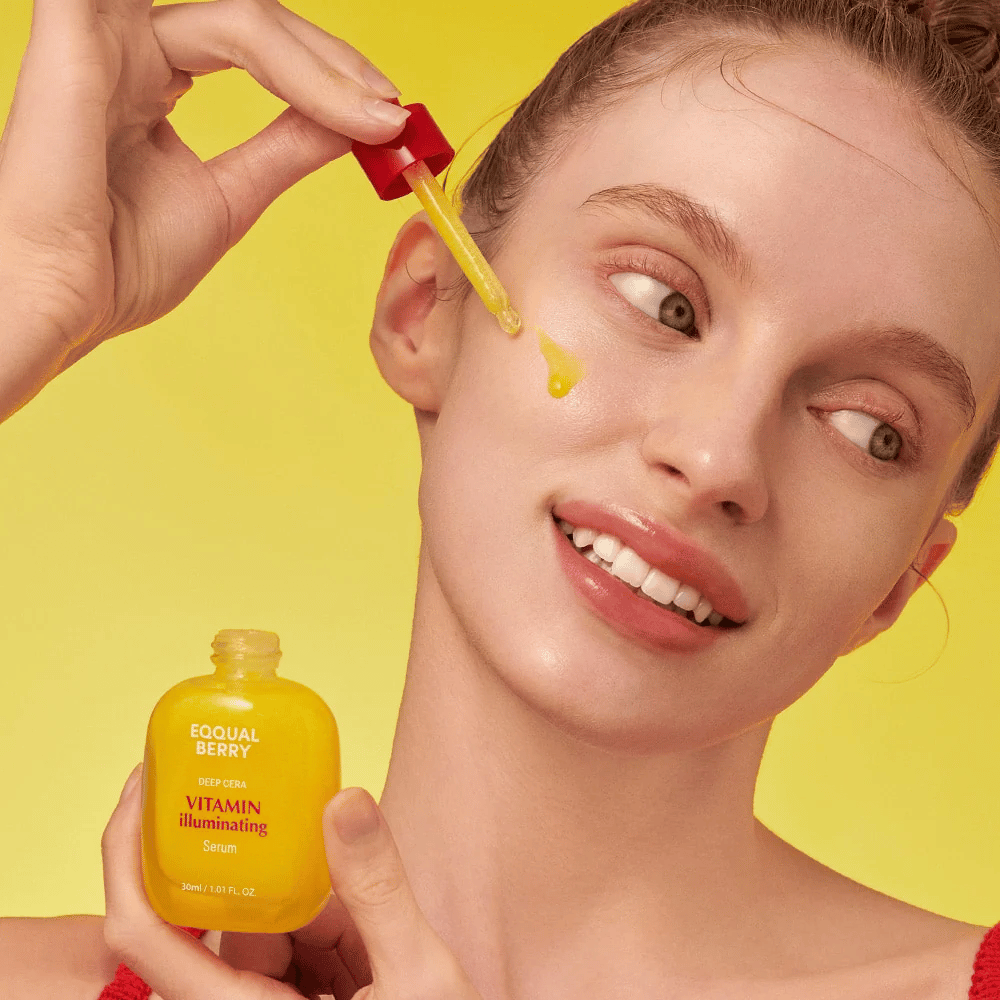 Smilende kvinde påfører Equal Berry Vitamin Illuminating Serum med en pipette. Frisk og strålende hud mod en livlig gul baggrund, der matcher serumets farve.